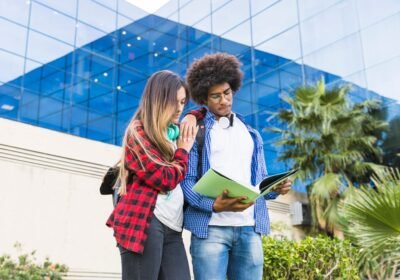 teenage-male-female-students-reading-book-standing-against-university-building_23-2148093514